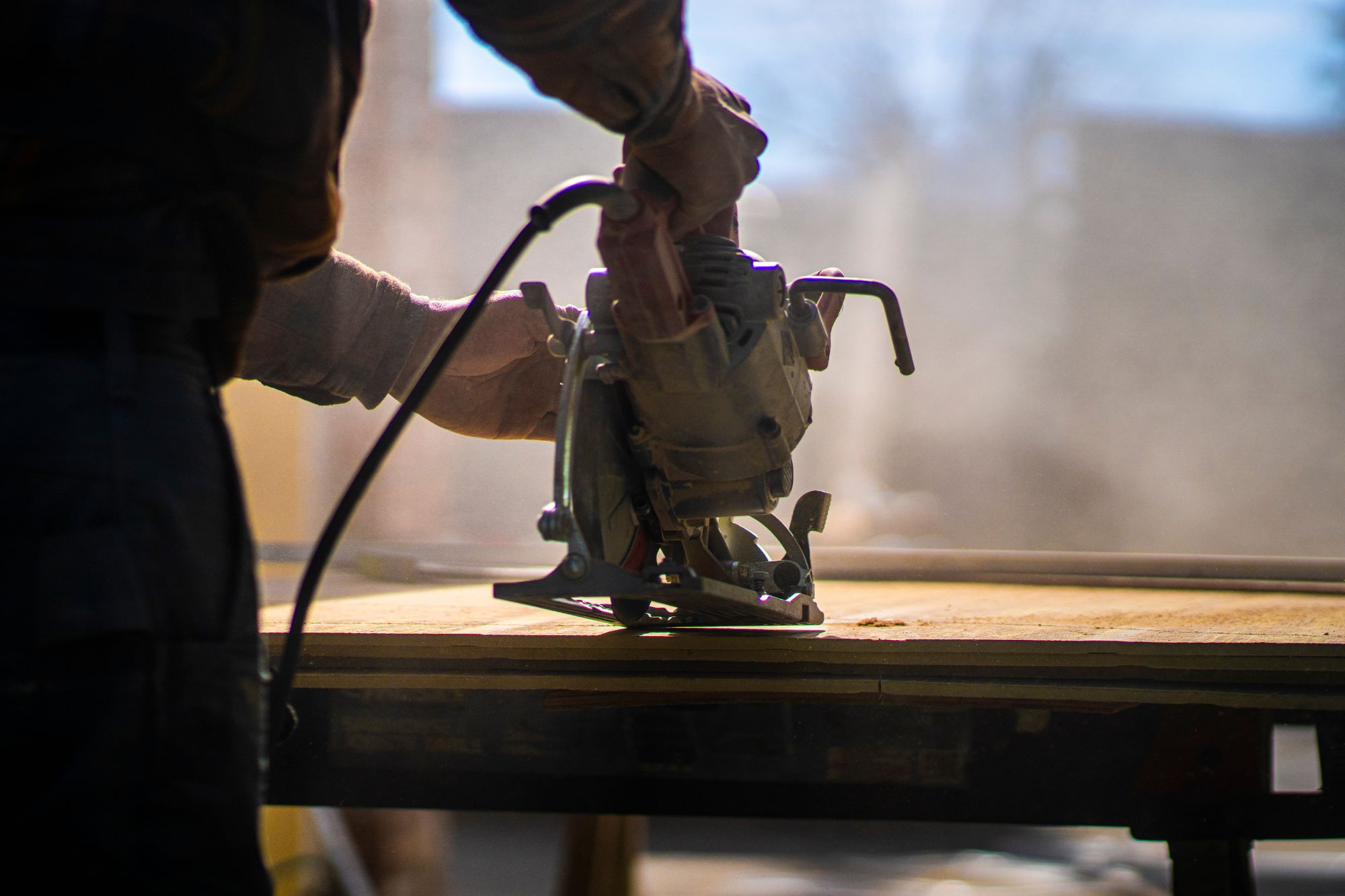 Skilled Hand Operating Circular Saw Cutting Wood Plank while wood dust flies